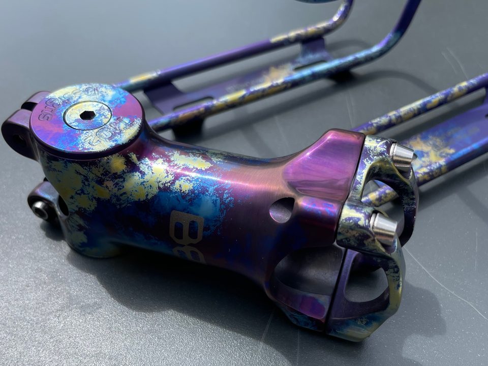 Titanium stem and top cap anodized in a violet, blue and gold splatter, with matching bottle cages behind