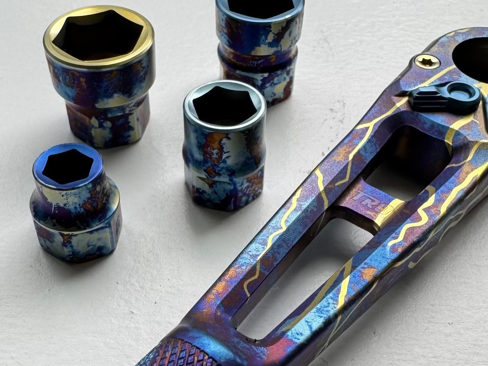 A titanium ratchet and four sockets anodized in a blue and purple splatter with gold inlay