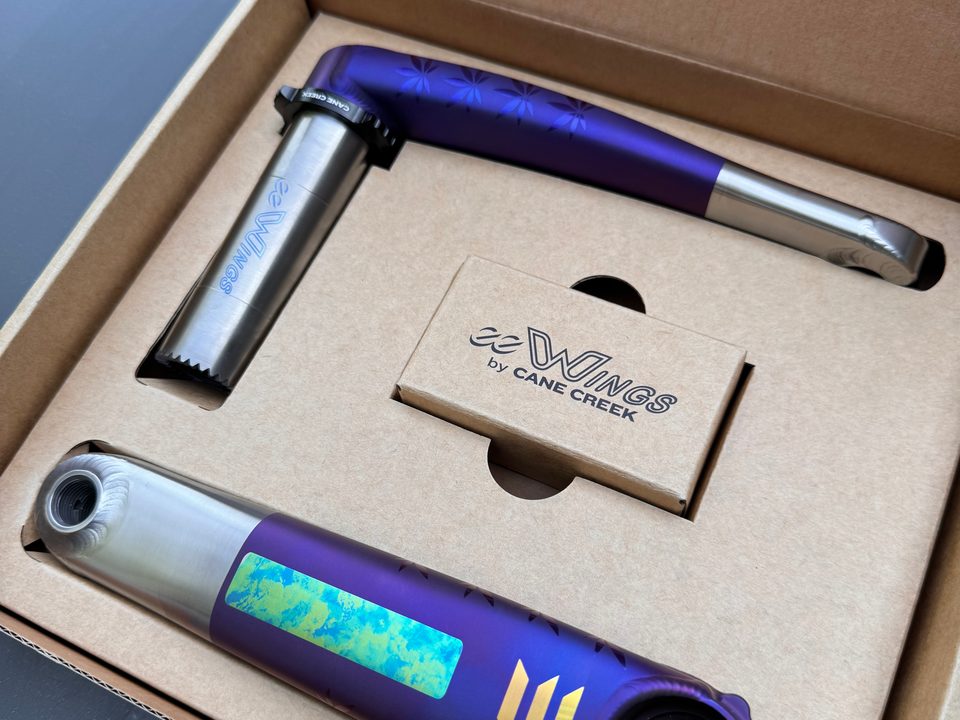 Violet anodized eeWings crank arms in their Cane Creek box, one with an iridescent panel and gold chevrons