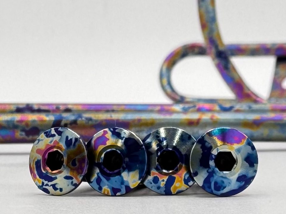 Four titanium bolts anodized in a splatter pattern, with matching bottle cages behind