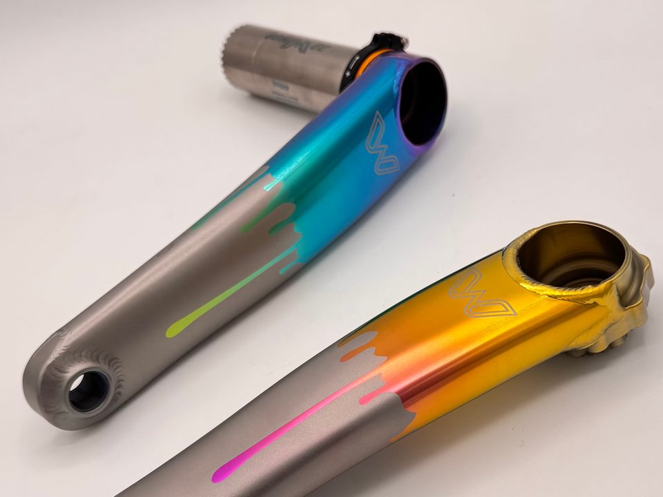 Cane Creek eeWings titanium crank arms anodized in blue-to-teal and gold fades with pink and green drips
