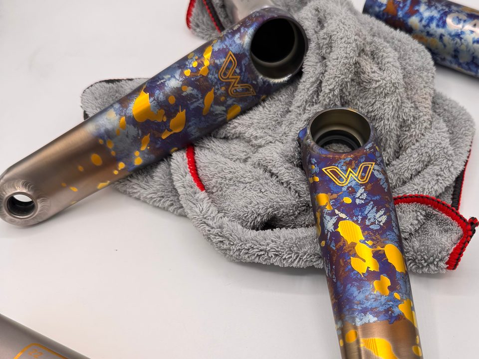 Two eeWings crank arms anodized in a blue and gold splatter, resting on a grey towel