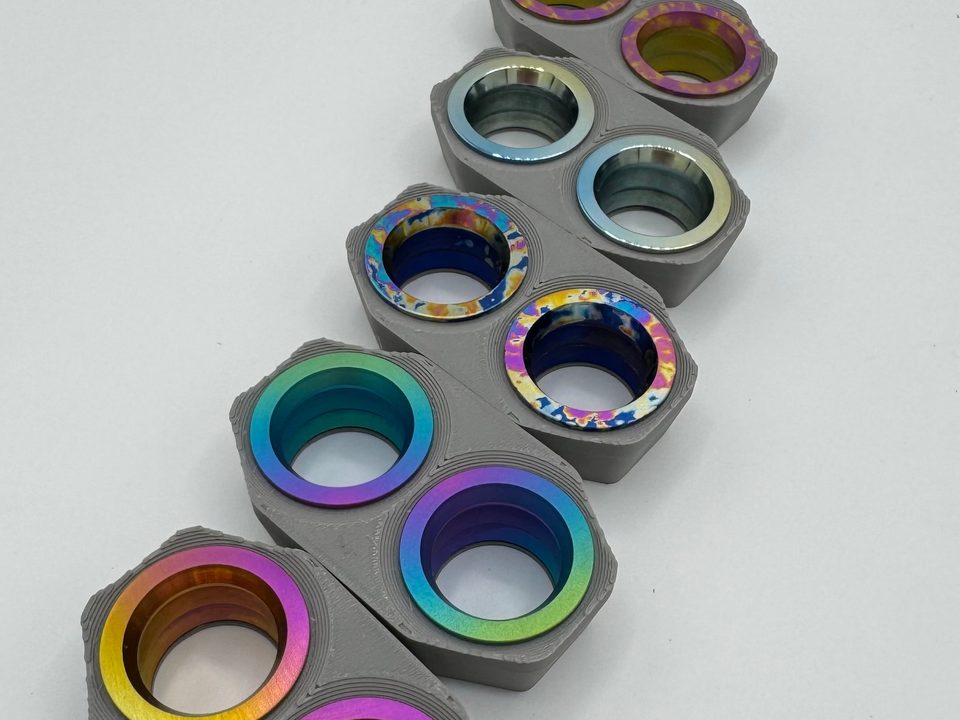 Five pairs of anodized titanium rings in fades and splatter, held in grey 3D-printed fixtures