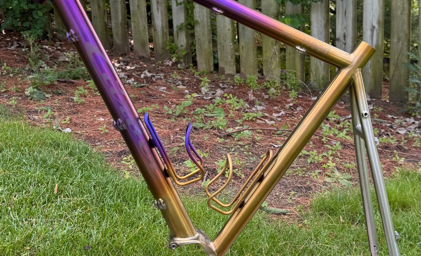 Titanium front triangle anodized in a purple-to-gold fade, with matching bottle cages
