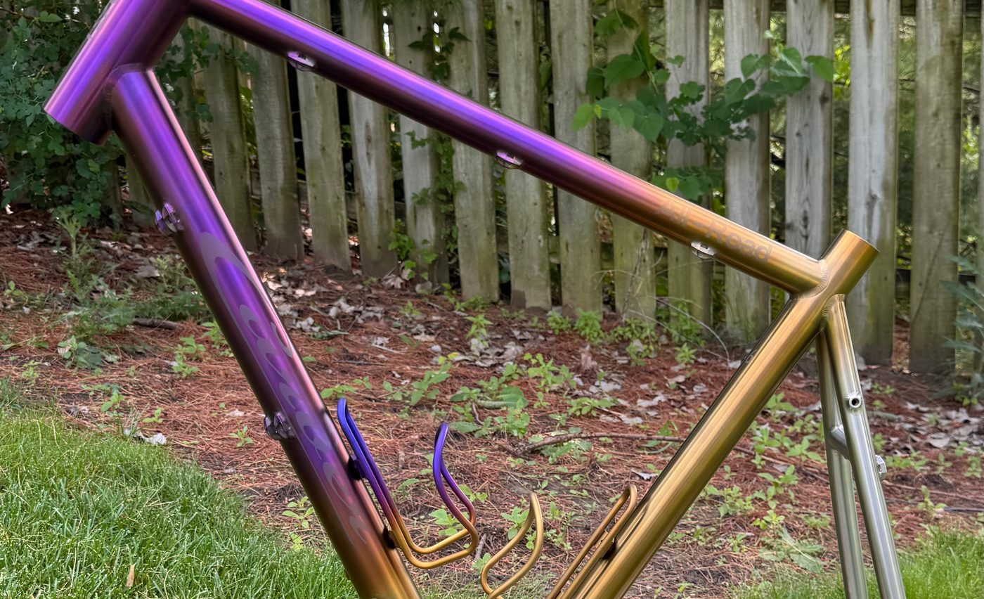 Titanium front triangle anodized in a purple-to-gold fade, with matching bottle cages