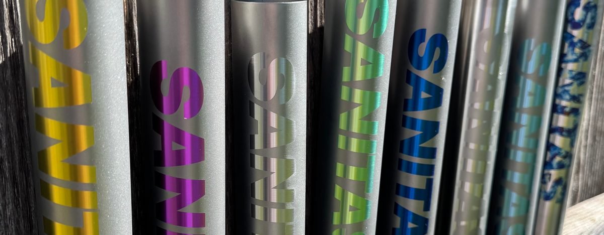 A row of titanium tubes, each with the SANITAS logo in a different anodized colour