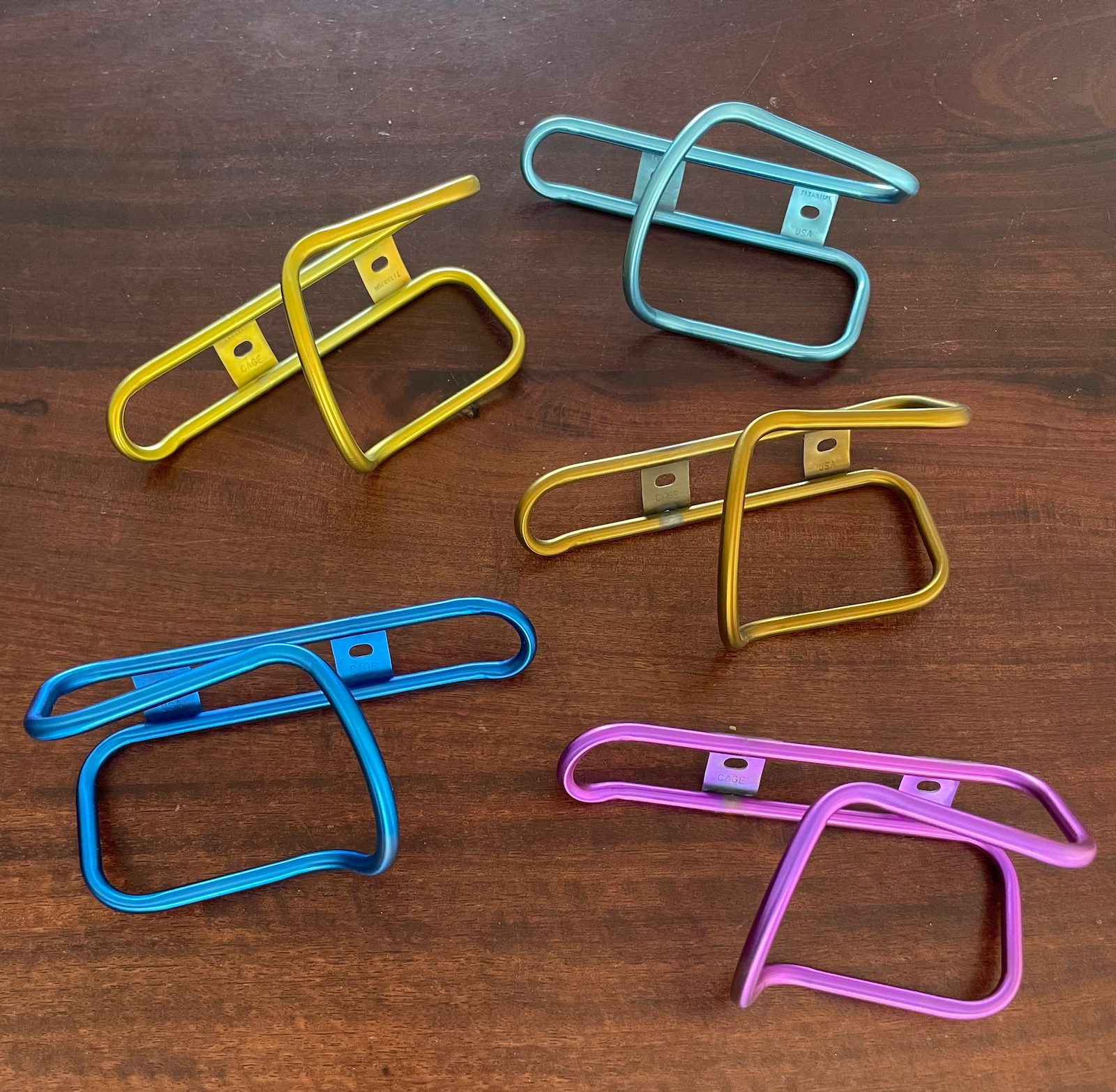Five King Cage titanium bottle cages anodized in solid yellow, teal, gold, blue and magenta