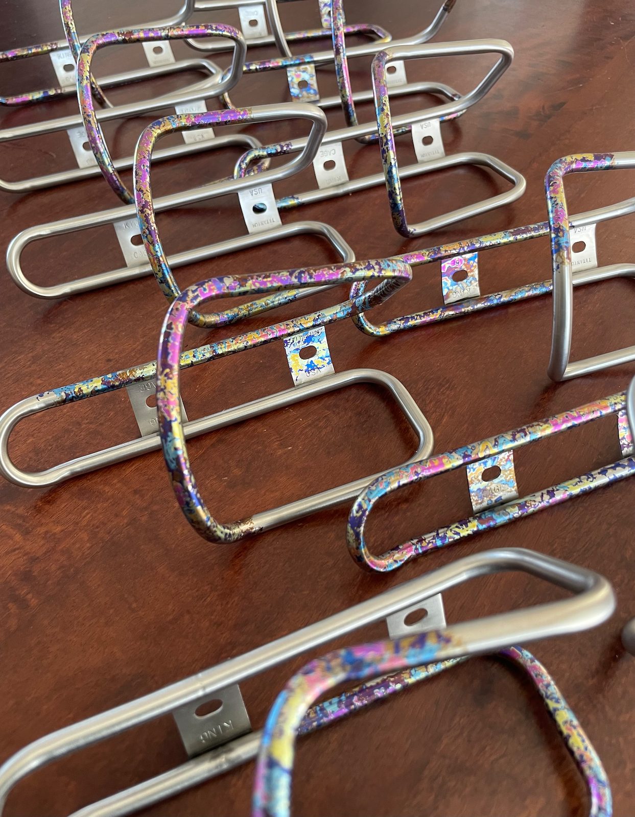 King Cage titanium bottle cages in the multi-color Ti-dye speckle finish beside unfinished raw cages